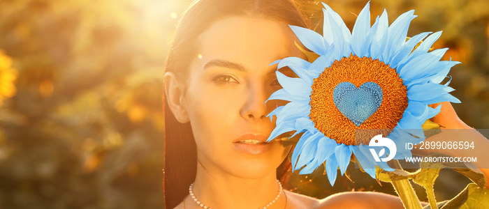 Beautiful young woman with sunflower in colors of Ukrainian flag on sunny day