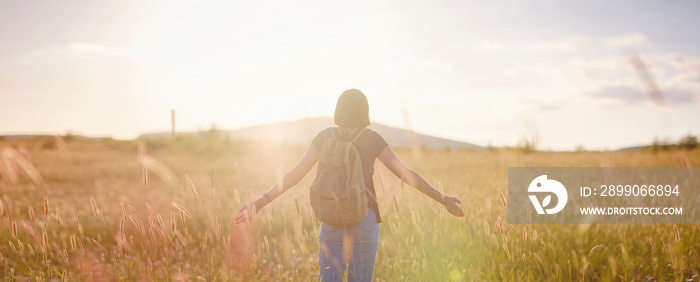 young woman with a backpack in a field at sunset