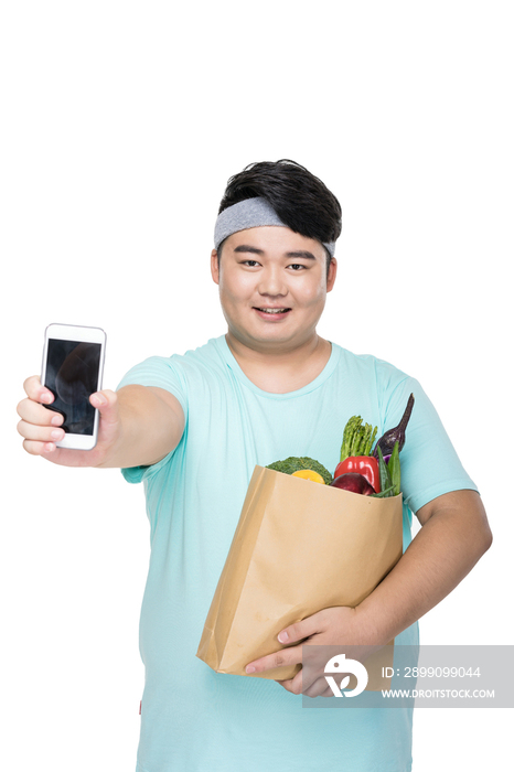 肥胖的年轻男子拿着手机和各种蔬菜