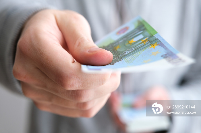 Male hand giving only one money banknote for a payment on white background, close up of caucasian adult man handing out European Union currency, euro. Selective focus on money.