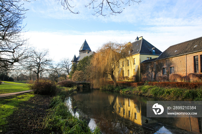 Panoramic view over moat on medieval water castle  and hunting lodge with bare trees in winter against blue sky - Krefeld Linn, Germany