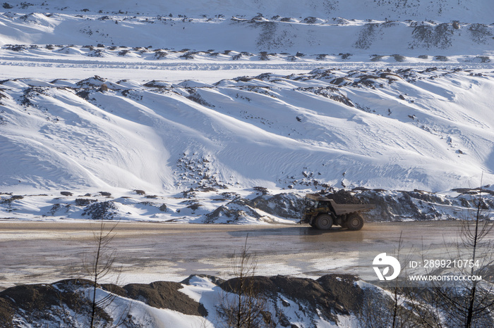 Loaded haul truck driving on a muddy road at an open pit mine in winter