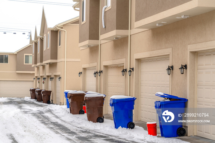 Exterior of apartments with garbage cans in front of the white garage doors