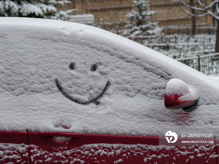 painted smiley face in the snow falling on the car window