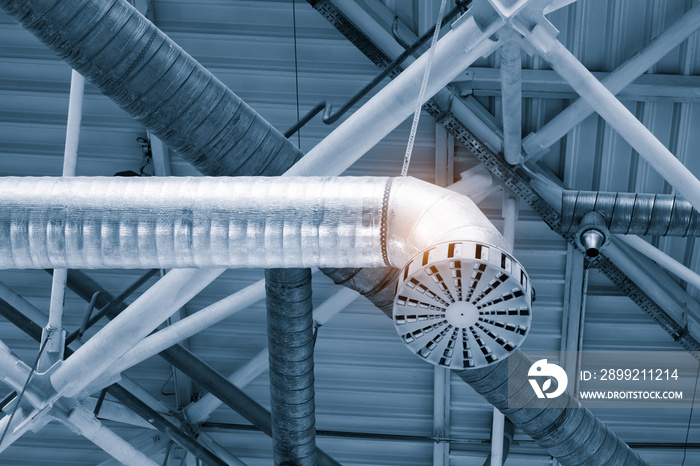 Ventilation pipes in silver insulation material hanging from the ceiling inside new building.