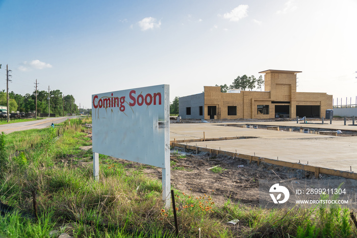 Coming Soon sign stands at the street corner/intersection, under construction convenience store is in background. Signboard with the words Coming Soon outdoor for brand new gas station soon open.