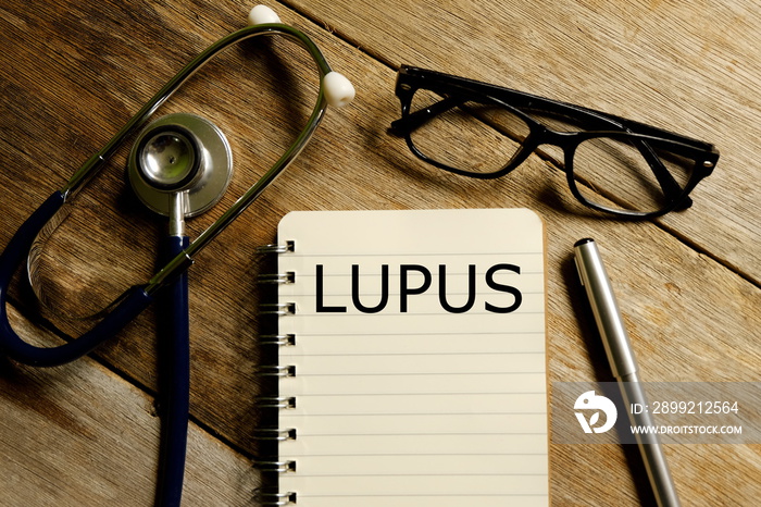 Top view of notebook written with LUPUS with stethoscope,pen and sunglasses on wooden background. Medical and healthcare theme.