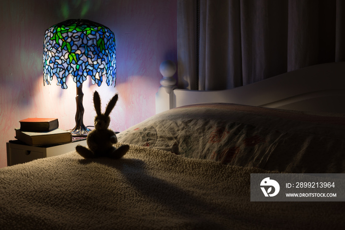 Toy rabbit back lit by Tiffany lamp in bedroom.