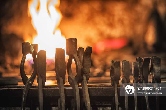 Blacksmith furnace with burning coals, tools, and glowing hot metal workpieces.