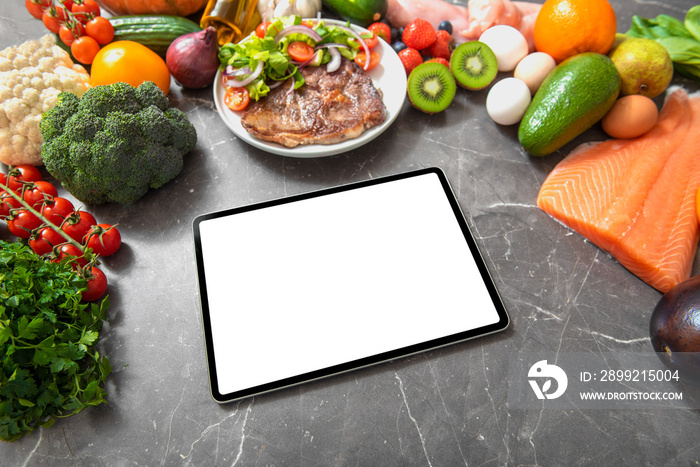 Tablet computer with white empty screen on a kitchen table surrounded by healthy products