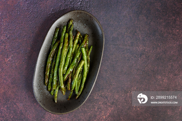 Freshly roasted whole green beans on a serving platter, with a rustic background