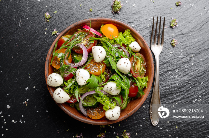 Flat lay of vegetable salad with mozzarella cheese, lettuce, cherry tomatoes, radish, cucumber, onion and basil in clay dish