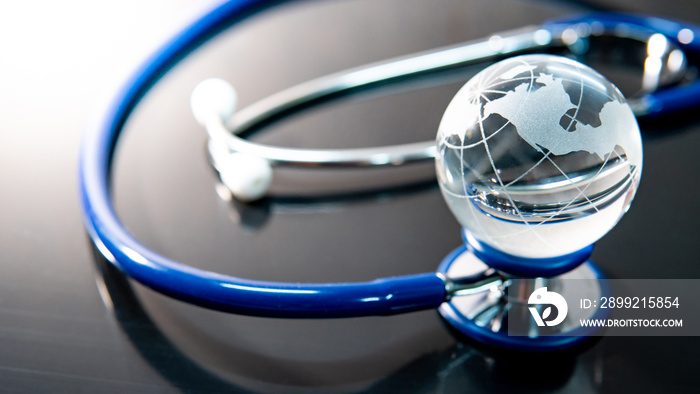 Global healthcare concept. World globe crystal glass on blue stethoscope on glossy desk. Health and medical science. Worldwide wellness business