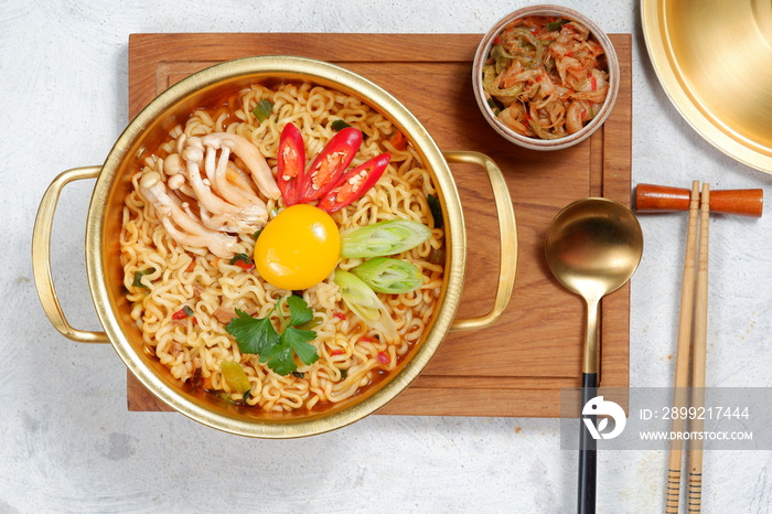 Serving a Korean style instant noodle, Ramyeon or Ramyun with spicy flavour topped with egg yolk, chilli, vegetables and kimchi in a traditional Korean noodle pot.