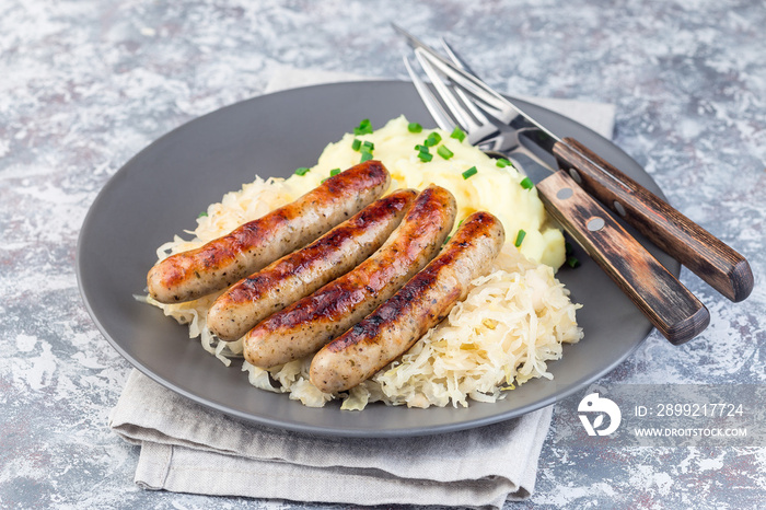 Roasted nuremberg sausages served with sour cabbage and mashed potatoes, on  gray plate, horizontal