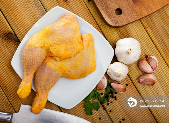 Raw poultry, fresh chicken legs quarters with condiments on wooden table