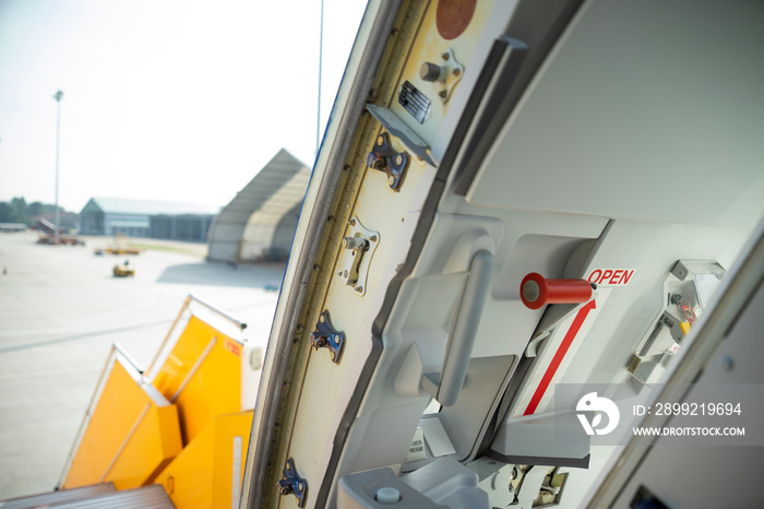 Open door to a large airliner as seen from inside. Aircraft door frame, door handle and door barrier strap