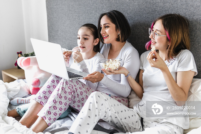 Hispanic women family enjoying live stream or watching a movie with computer or laptop on bed together mother and daughters in Latin America