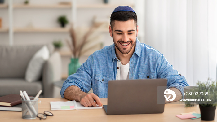 Smiling israeli man working on laptop at home