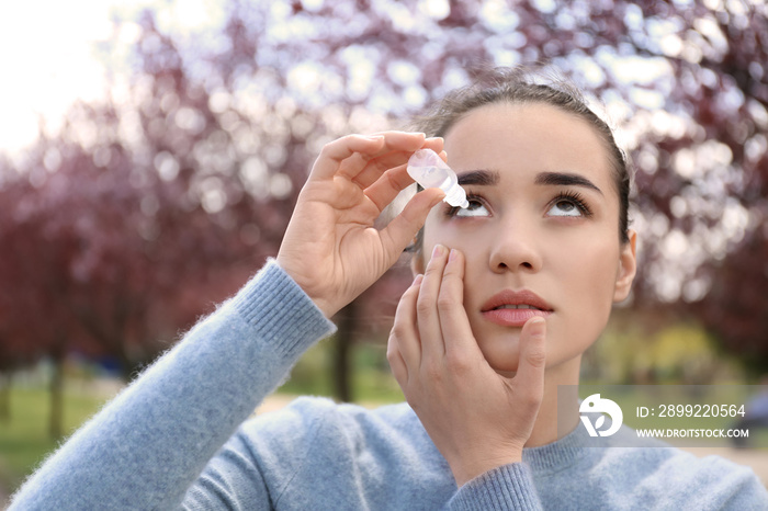 Young woman using eye drops near blooming trees. Allergy concept