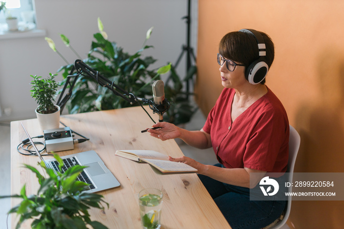 Middle-aged female radio presenter talking into the microphone and reading news - radio broadcast online concept