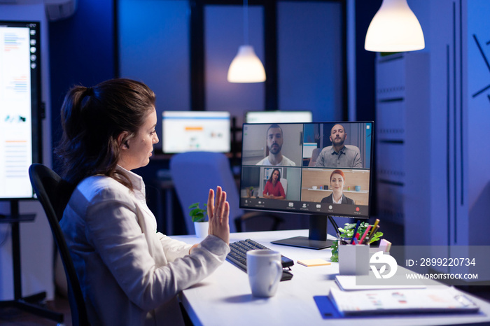 Back view of business woman talking about sale report in video conference working overtime in start-up office. Team using online wireless communication discussing on webcam during group meeting.