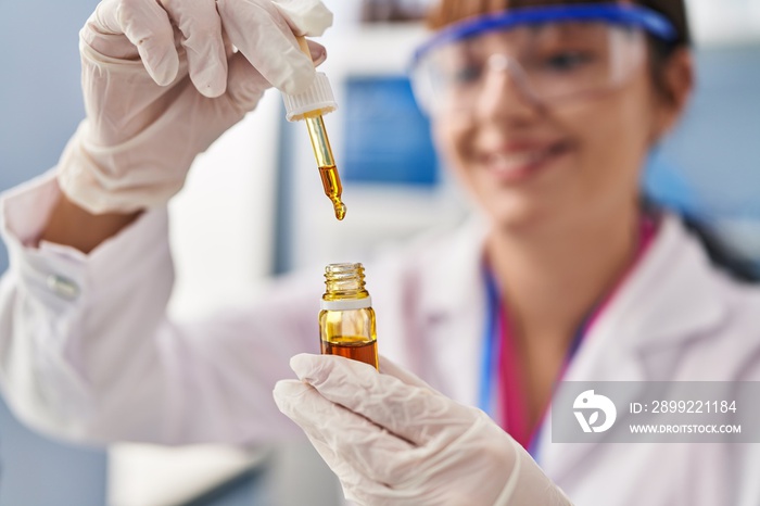 Young beautiful hispanic woman scientist holding bottle with liquid at pharmacy