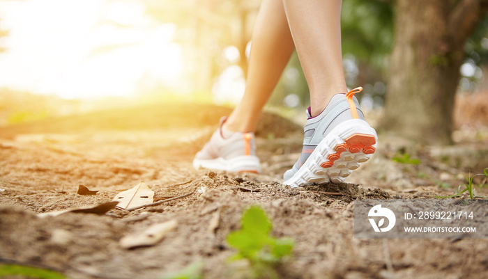 Woman runner in sneakers during run on trail in forest. Cropped