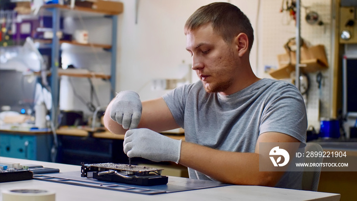 Electronic engineer of computer technology at work. Repairman repairs computer graphics card chipset in workshop. He is unscrewing the bolts sits at table. PC repair technician and electronic devices.