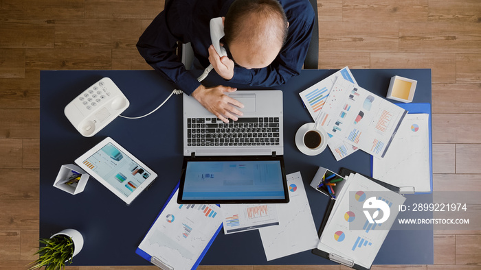 Top view of manager man planning company strategy typing management statistics on laptop computer. Businessman discussing financial graph at phone while working in business startup office