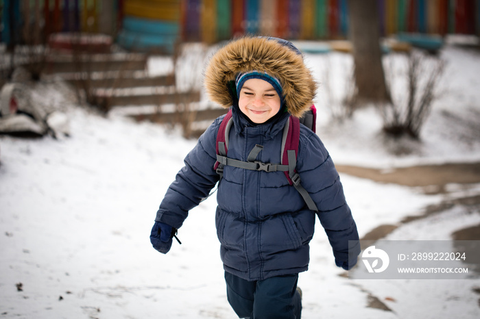 Smiling preschool boy running in warm coat with hood in winter outdoors