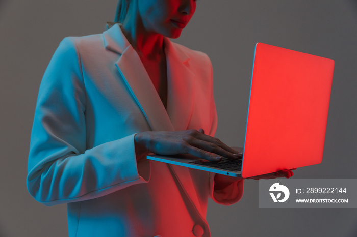 Image closeup of trendy woman 20s holding and working on laptop while standing under neon lights