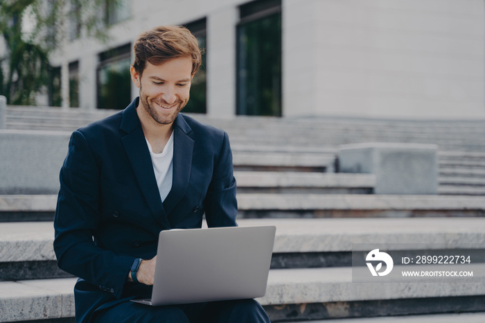 Young businessman sits on steps uses laptop organizes meeting online with investors