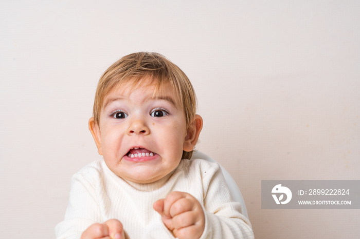 Toddler baby sitting on the high chair and doing funny grimace. Teeth of the baby. Face expression