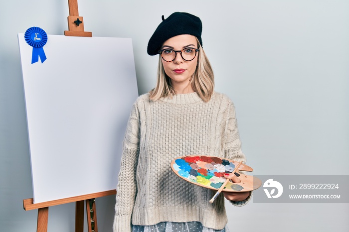 Beautiful caucasian woman drawing with palette on easel stand winner first place thinking attitude and sober expression looking self confident