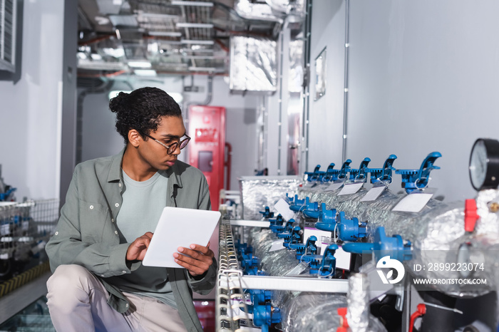 young afican american technician with digital tablet looking at cooling system of data center