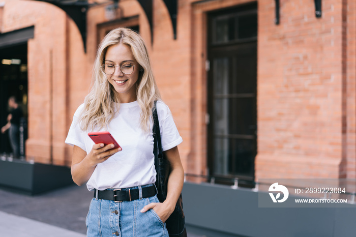 Cheerful woman with smartphone smiling on street