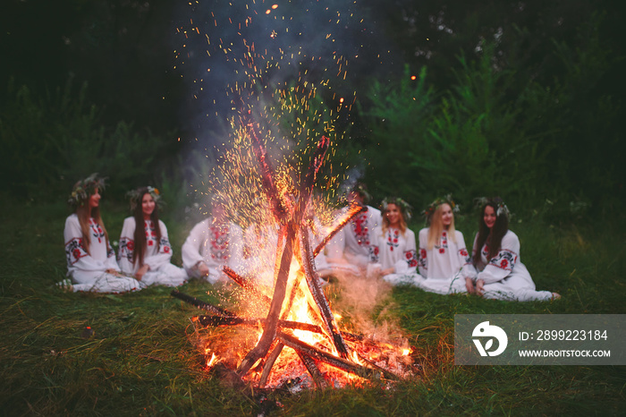 Midsummer night. Young people in Slavic clothes sitting near the bonfire.