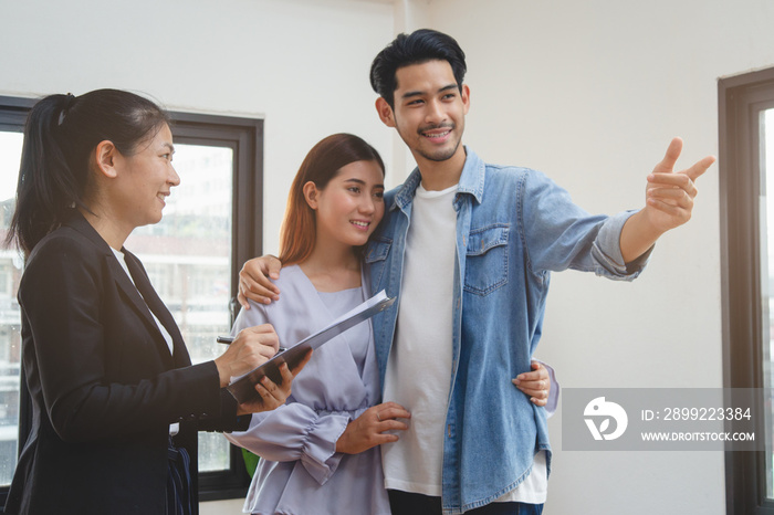 new house / home moving and relocation concept. Happy asian couple receiving apartment key from real estate agent / realtor.