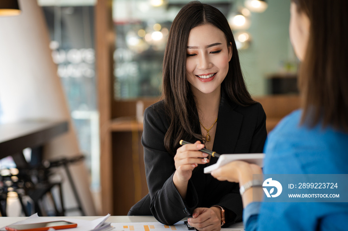 Two happy female Asian accountants counting on calculator income for tax form completion.