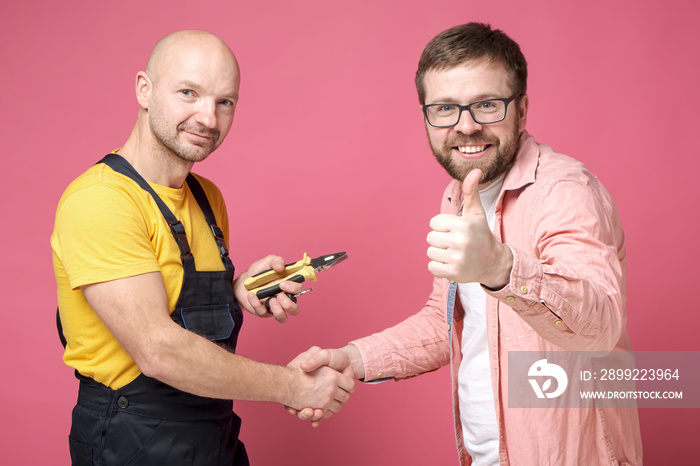 Grateful client makes a handshake with a worker and showing gesture thumb upwards, looking at the camera and smiling.