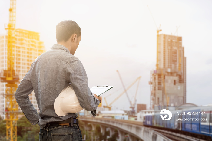 civil engineer holding helmet and working checklist construction with building construction and crane construction background