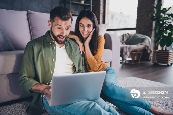 Portrait of beautiful handsome cheerful amazed couple sitting on carpet using laptop at home house flat indoors