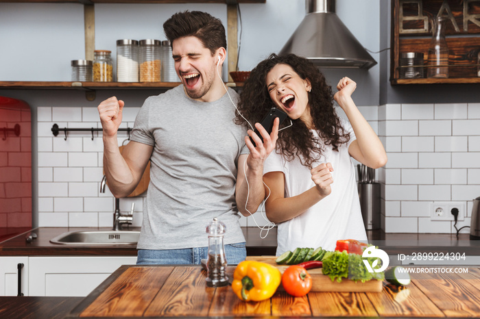 Portrait of cheery couple listening to music together while cooking salat in kitchen at home