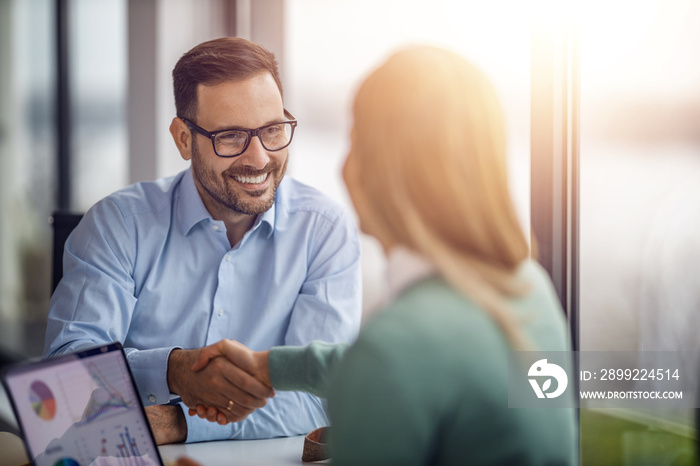 Two business people shaking hands while sitting at the working place