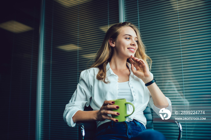 Successful executive manager with coffee cup dreaming during work break in office interior, happy female employee resting in modern company and dreaming about competitive professionalism at job