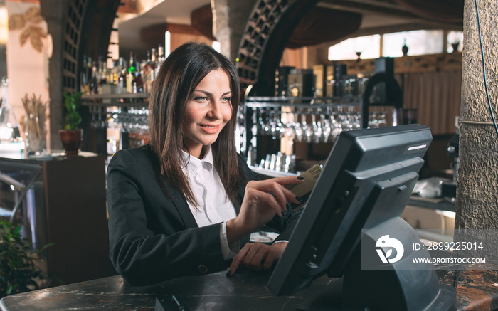 small business, people and service concept - happy woman or waiter or manager in apron at counter with cashbox working at bar or coffee shop