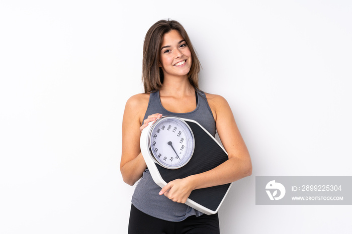 Teenager Brazilian girl holding a scale over isolated white background with weighing machine