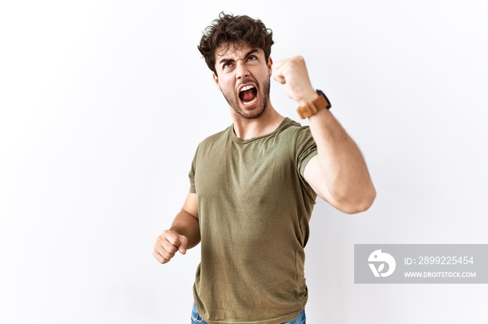 Hispanic man standing over isolated white background angry and mad raising fist frustrated and furious while shouting with anger. rage and aggressive concept.