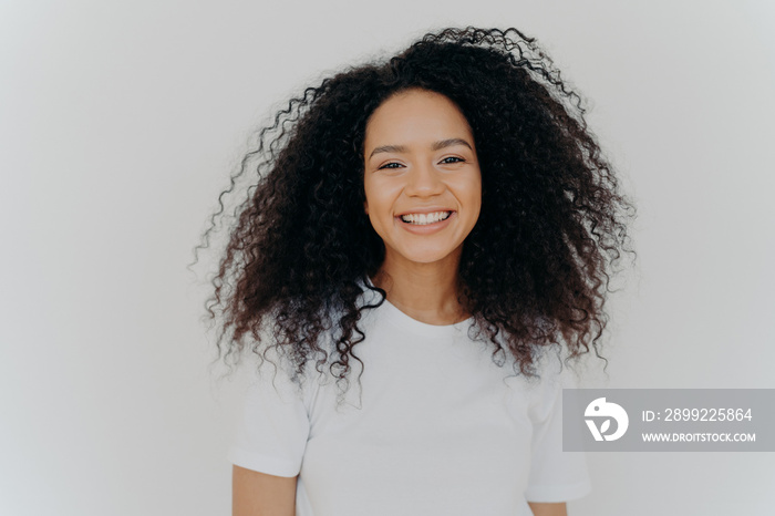 Pleasant looking young woman has toothy smile, happy face expression, laughs at something funny, shows white perfect teeth, dressed casually, isolated over white background, glad to start new life